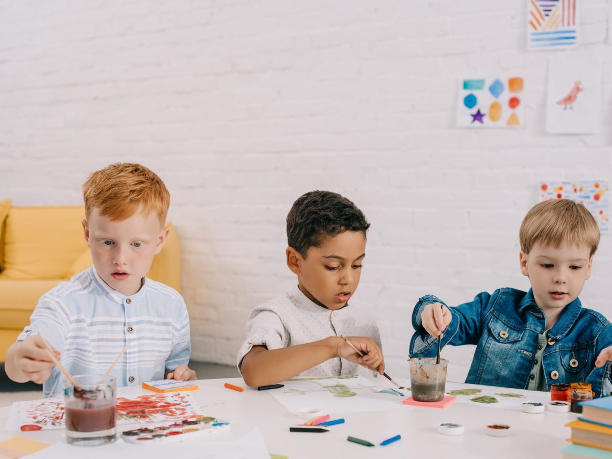 portrait of multiethnic kids with paint brushes drawing pictures in classroom